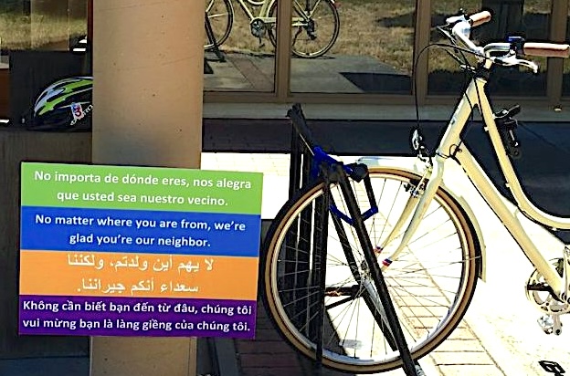 "No matter where you are from, we're glad you're our neighbor," states a sign in 4 languages. It is next to a bike rack at a Monterey church.